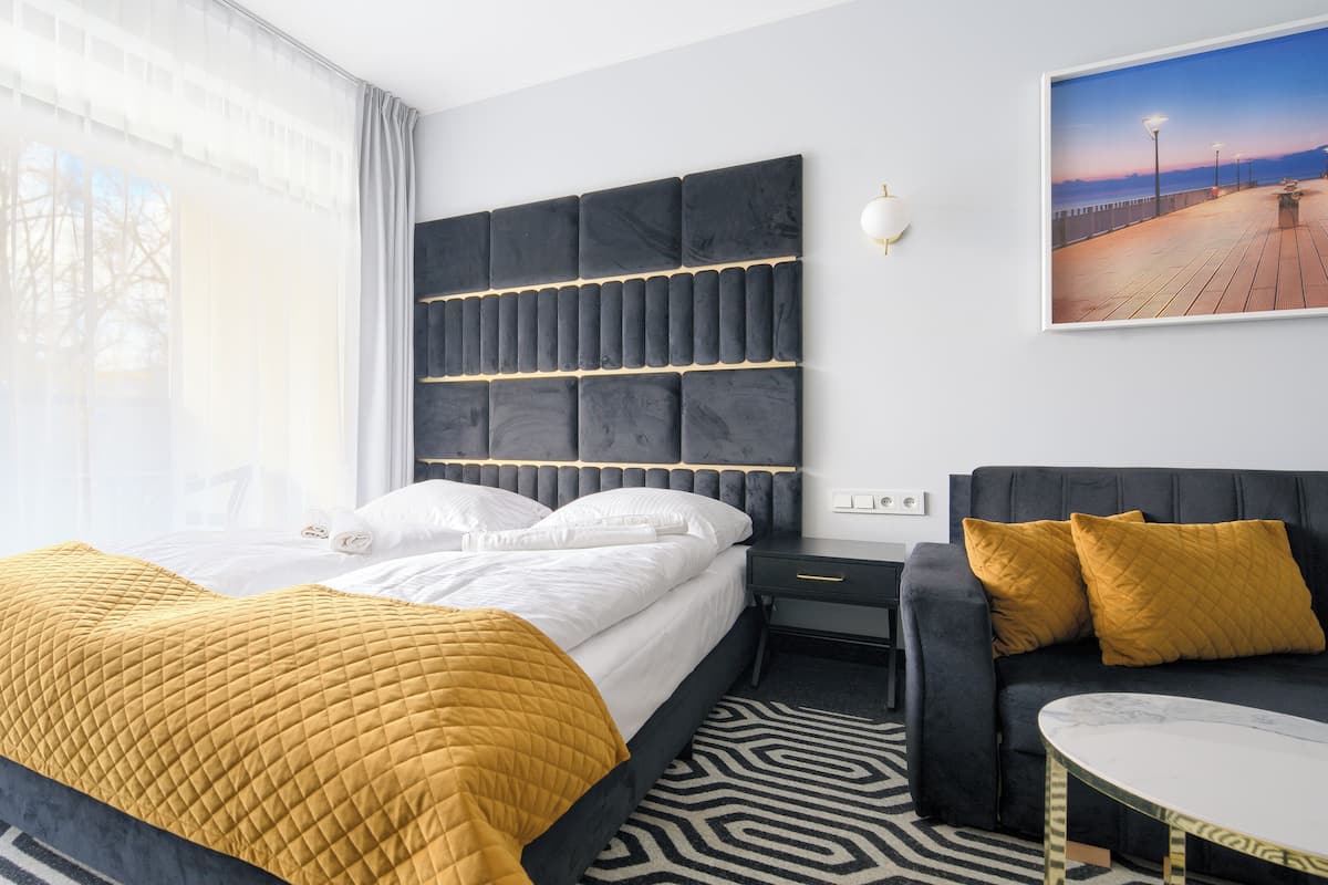 A modern hotel room with a large bed, a sofa, and a view of a sunset over a body of water.