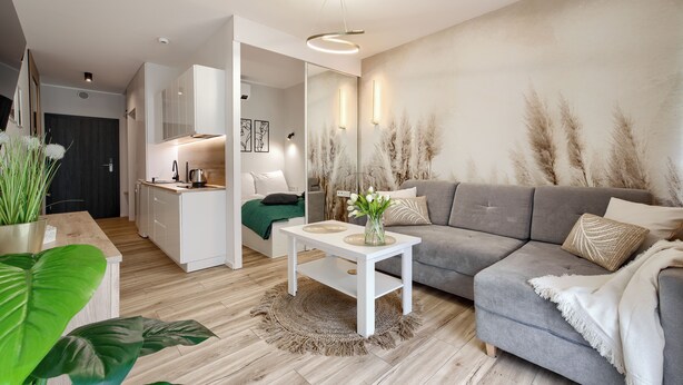 A modern living room with a grey sofa, a white coffee table, and a kitchen area with white cabinets. - Apartamenty Sun & Snow Solny Resort (Kolobrzeg)
