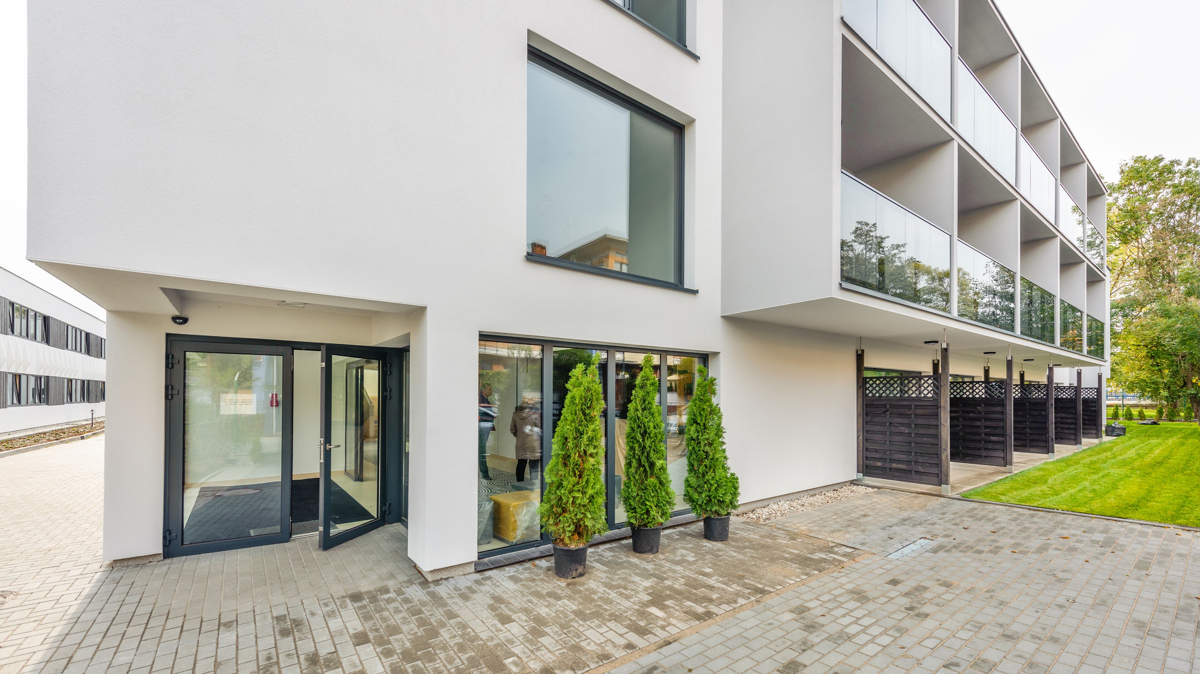 Um edifício moderno com entrada de vidro, plantas em vasos e um calçadão pavimentado.