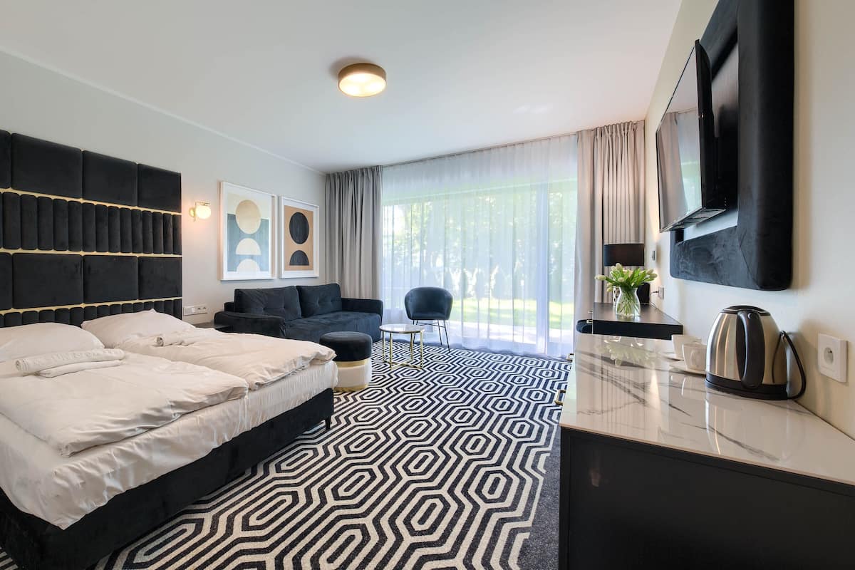 A modern hotel room with a large bed, a sofa, a coffee table, and a TV mounted on the wall.