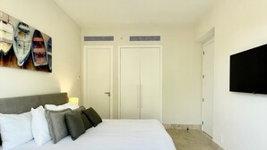 A bedroom with a bed, a ceiling fan, a TV mounted on the wall, and a painting of boats. - Deluxe 2BR Marina Dockside Dreams (Río Hato)