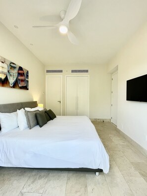 A bedroom with a bed, a ceiling fan, a TV mounted on the wall, and a painting of boats. - Deluxe 2BR Marina Dockside Dreams (Río Hato)