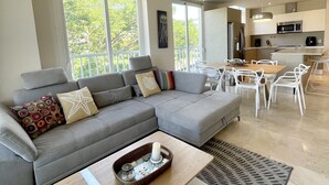 A modern living room with a grey sectional sofa, a dining table with chairs, and a kitchen area with a microwave and refrigerator. - Deluxe 2BR Marina Dockside Dreams (Río Hato)