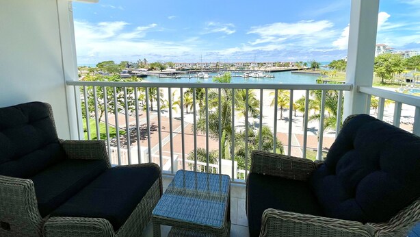 A balcony with wicker furniture and a view of a marina and beach. - Deluxe 2BR Marina Dockside Dreams (Río Hato)