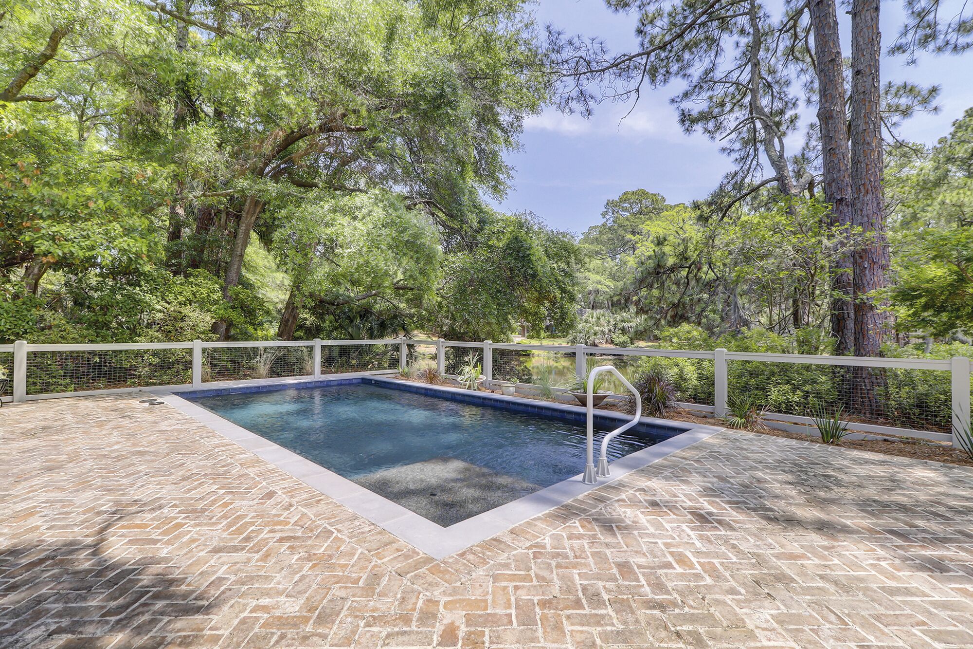 Une piscine rectangulaire, dotée d’une terrasse et d’une clôture blanches, le tout situé dans un espace boisé.