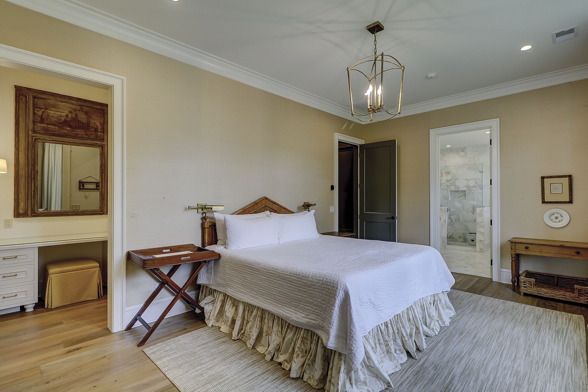 A bedroom with a large bed, a wooden nightstand, a mirror, a door, and a small table with a lamp.
