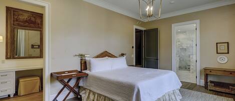 A bedroom with a large bed, a wooden nightstand, a mirror, a door, and a small table with a lamp.