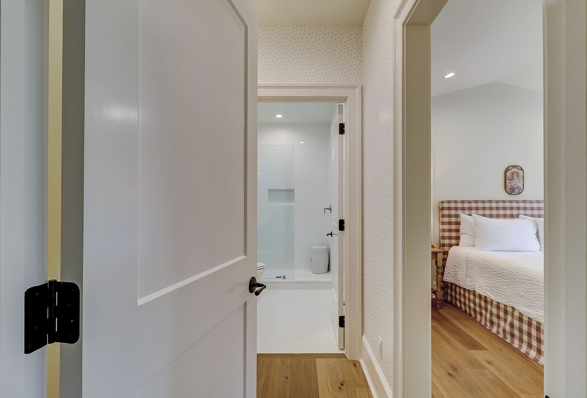Une chambre d’hôtel avec une couvre-lit à carreaux, un mur blanc orné d’un petit tableau et un plancher en bois.