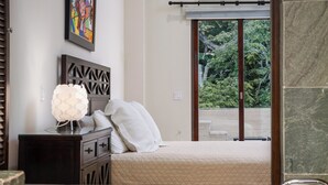 Un dormitorio con una cama, una mesita de noche, una lámpara y una ventana con vistas a árboles.