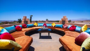Un espacio de estar circular con una mesa en el centro, rodeado de cojines de colores y una vista despejada del paisaje.