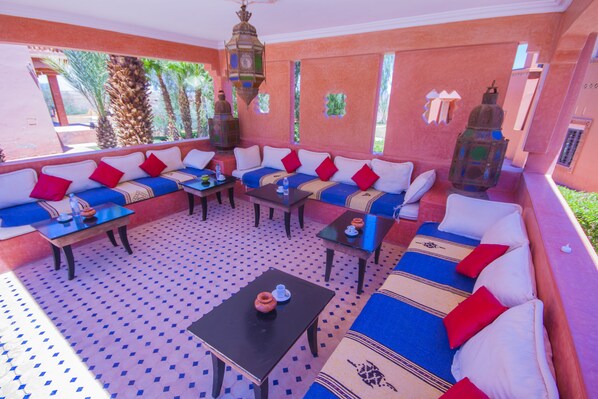Una habitación con piso estampado, un sofá con cojines rojos y blancos, una mesa con un florero y un farol colgante.