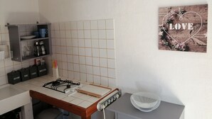 A kitchen with a gas stove, a sink, a cabinet with kitchen utensils, and a wall-mounted picture of a heart with the word "LOVE". - Charming studio 25 min from vallon pont d'arc (Le Garn)