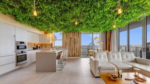 A modern kitchen with white cabinets and stainless steel appliances, a wooden dining area, and a living space with a white sofa and a coffee table. - Skyline Views 2BR w/ Pool Hollywood (Hollywood)