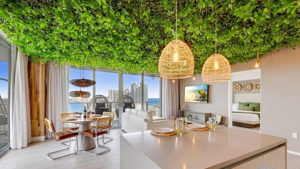 A modern kitchen with a central island, dining area with chairs, and a view of the city skyline. - Skyline Views 2BR w/ Pool Hollywood (Hollywood)
