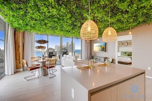 A modern kitchen with a central island, dining area with chairs, and a view of the cityscape through large windows. - Skyline Views 2BR w/ Pool Hollywood (Hollywood)