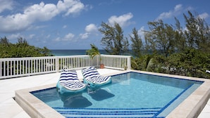 Una piscina rettangolare con piastrelle blu, due lettini a righe e un parapetto bianco.