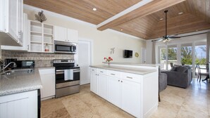 Una cucina moderna con mobili bianchi, un'isola centrale, elettrodomestici in acciaio inossidabile e un soffitto in legno.