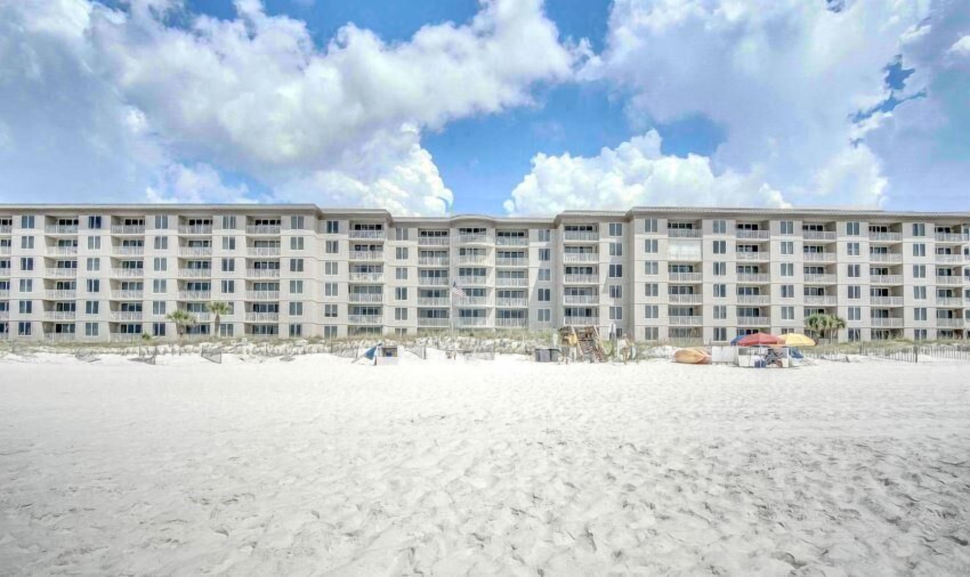 Een hotel aan het strand met meerdere verdiepingen, balkons en een zandstrand ervoor.