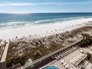 A beach view with a pool area, lounge chairs, and a clear sky.