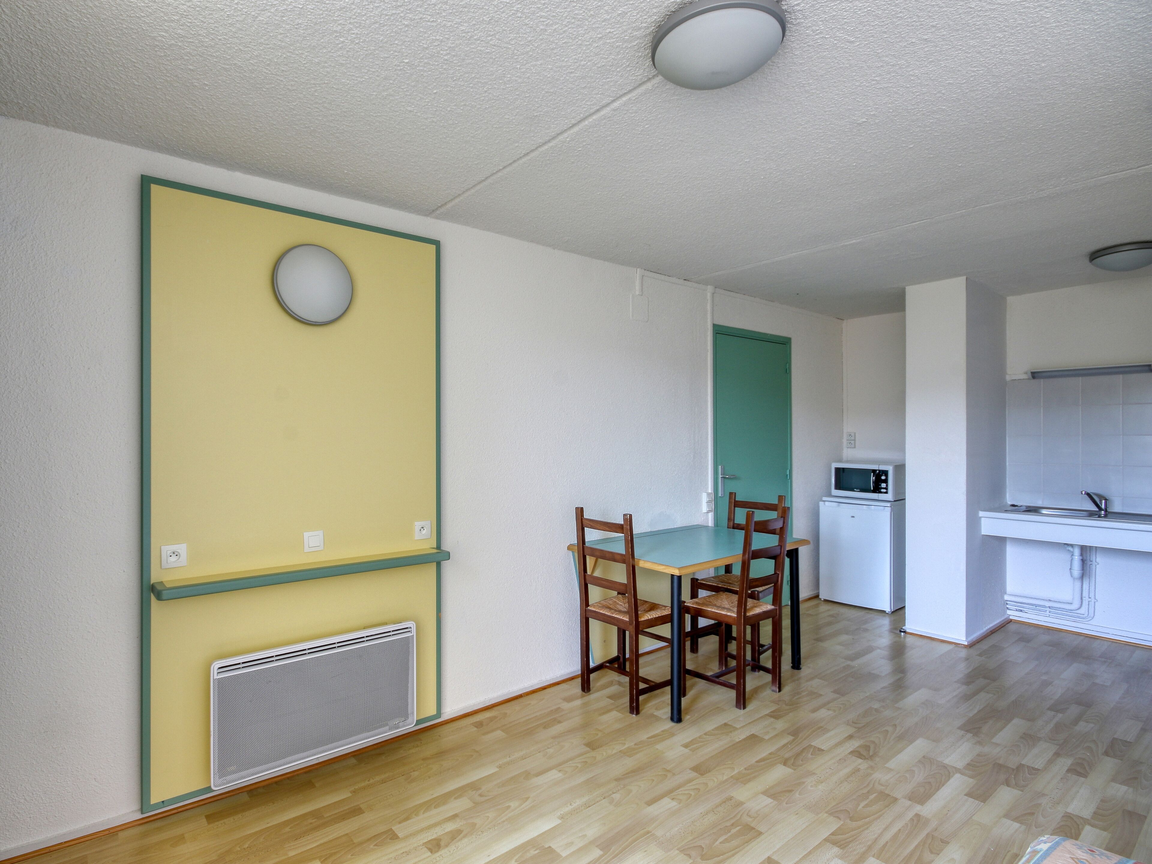 A room with a dining table, chairs, a microwave, and a kitchenette.