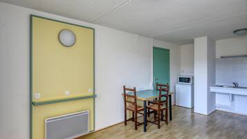 A room with a dining table, chairs, a microwave, and a kitchenette.