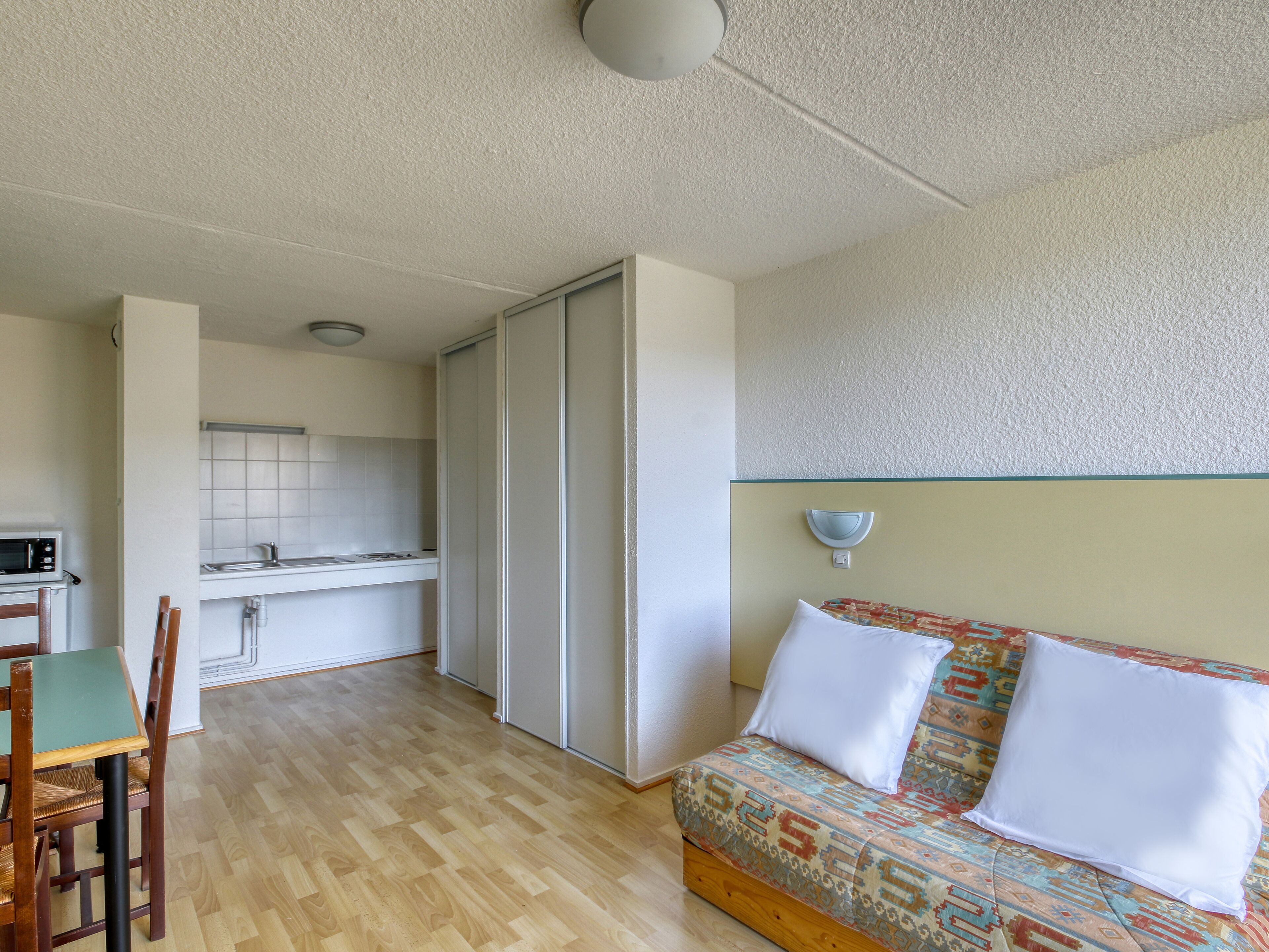 Un espacio habitable pequeño con kitchenette, un sofá de tapicería estampada y una zona de comedor con mesa y sillas de madera.