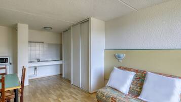 Un espacio habitable pequeño con kitchenette, un sofá de tapicería estampada y una zona de comedor con mesa y sillas de madera.