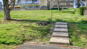 A grassy area with a concrete pathway leading to a building with a stone facade and large windows. - Vacancéole - Le Domaine de Confolant (Miremont)