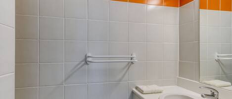 Un baño con baldosas blancas y anaranjadas, un lavamanos blanco, un espejo y un perchero para toallas.
