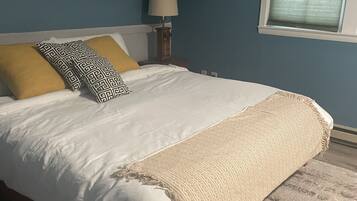 A bedroom with a bed, pillows, a nightstand, a lamp, and a window.