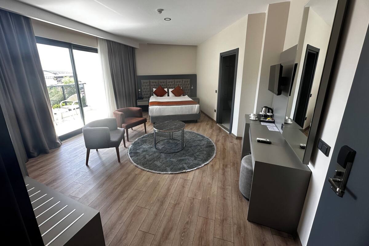 Ein Hotelzimmer mit Bett, Schreibtisch, Stuhl, Fernseher und einem Balkon mit Vorhängen.