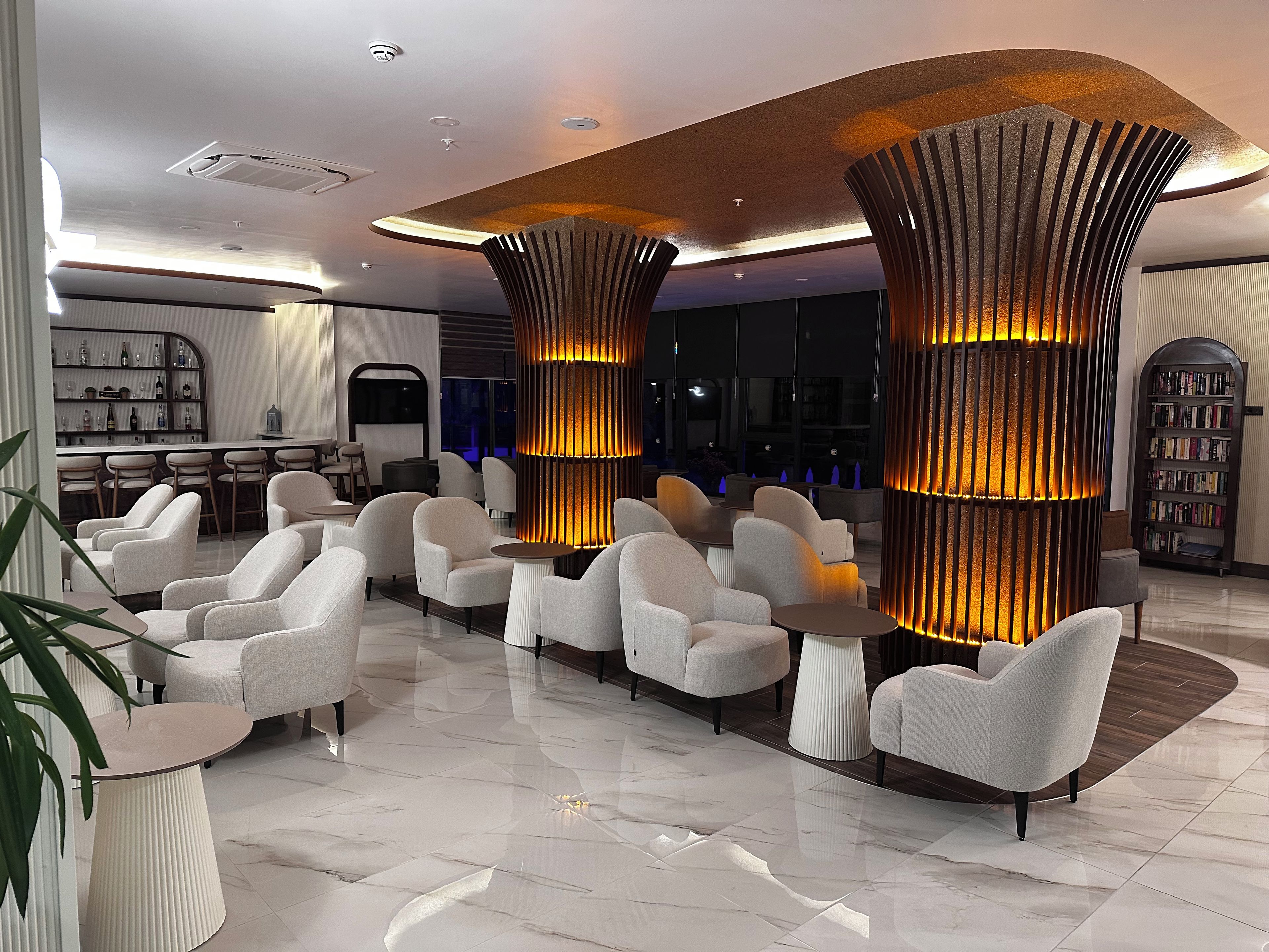 A modern lobby with a bar area, seating with tables, and a large bookshelf.