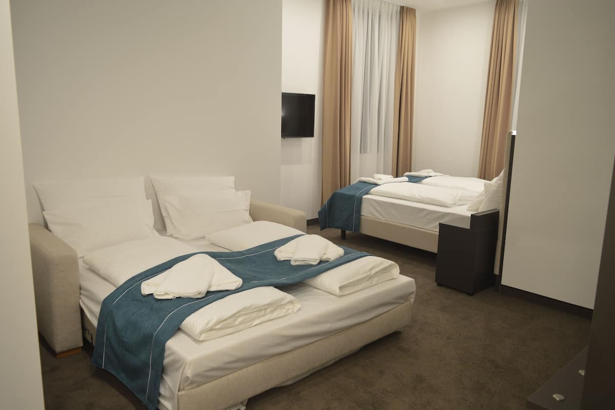 Habitación de hotel con dos camas, un televisor de pantalla plana y un ventanal grande con cortinas.