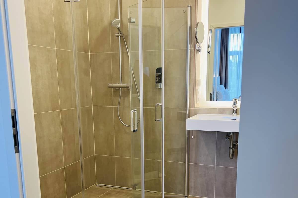 Un baño moderno con ducha envuelta en vidrio, lavamanos blanco y espejo.