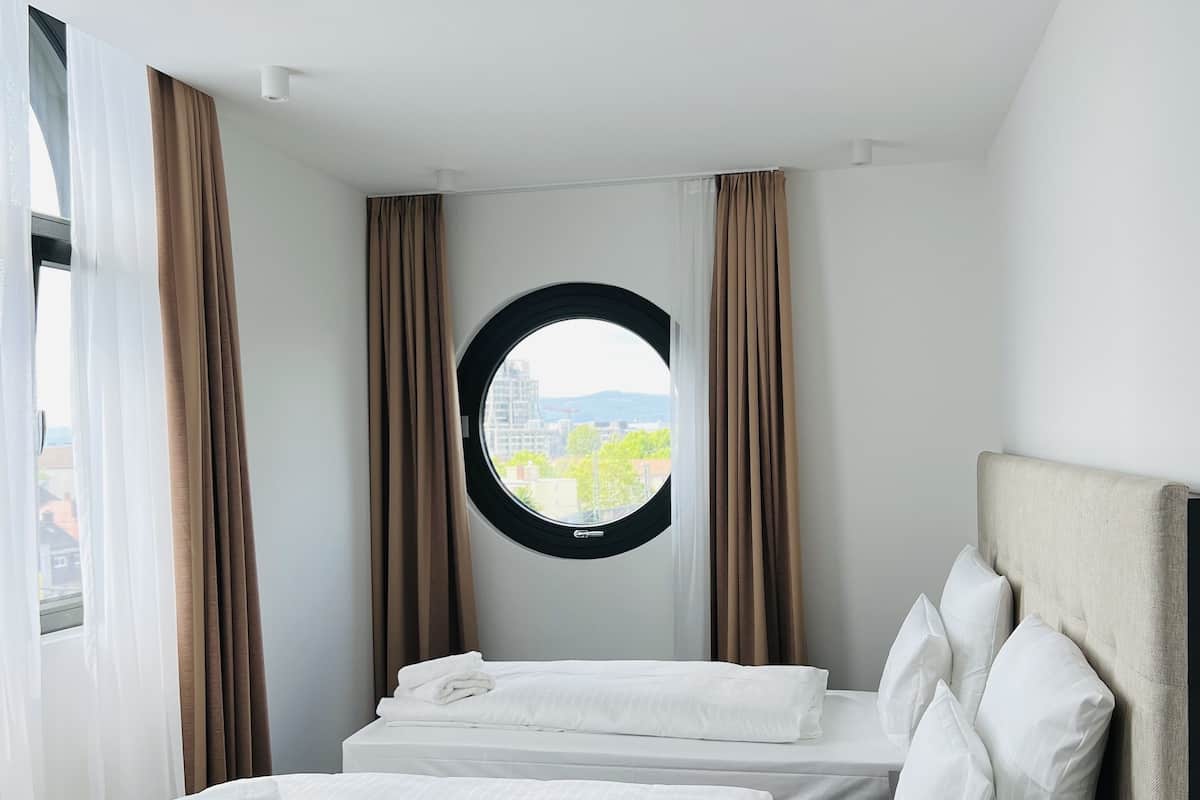Habitación de hotel con una cama grande, dos almohadas, un ventanal redondo y cortinas.