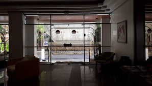 A hotel lobby with a large glass entrance, a reception desk, and seating areas. - Apartment with beautiful sea view - Praia de Pitangueiras (Guarujá)