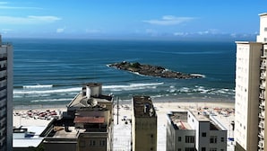 A coastal cityscape with a beach, buildings, and a rocky outcrop in the sea. - Apartment with beautiful sea view - Praia de Pitangueiras (Guarujá)
