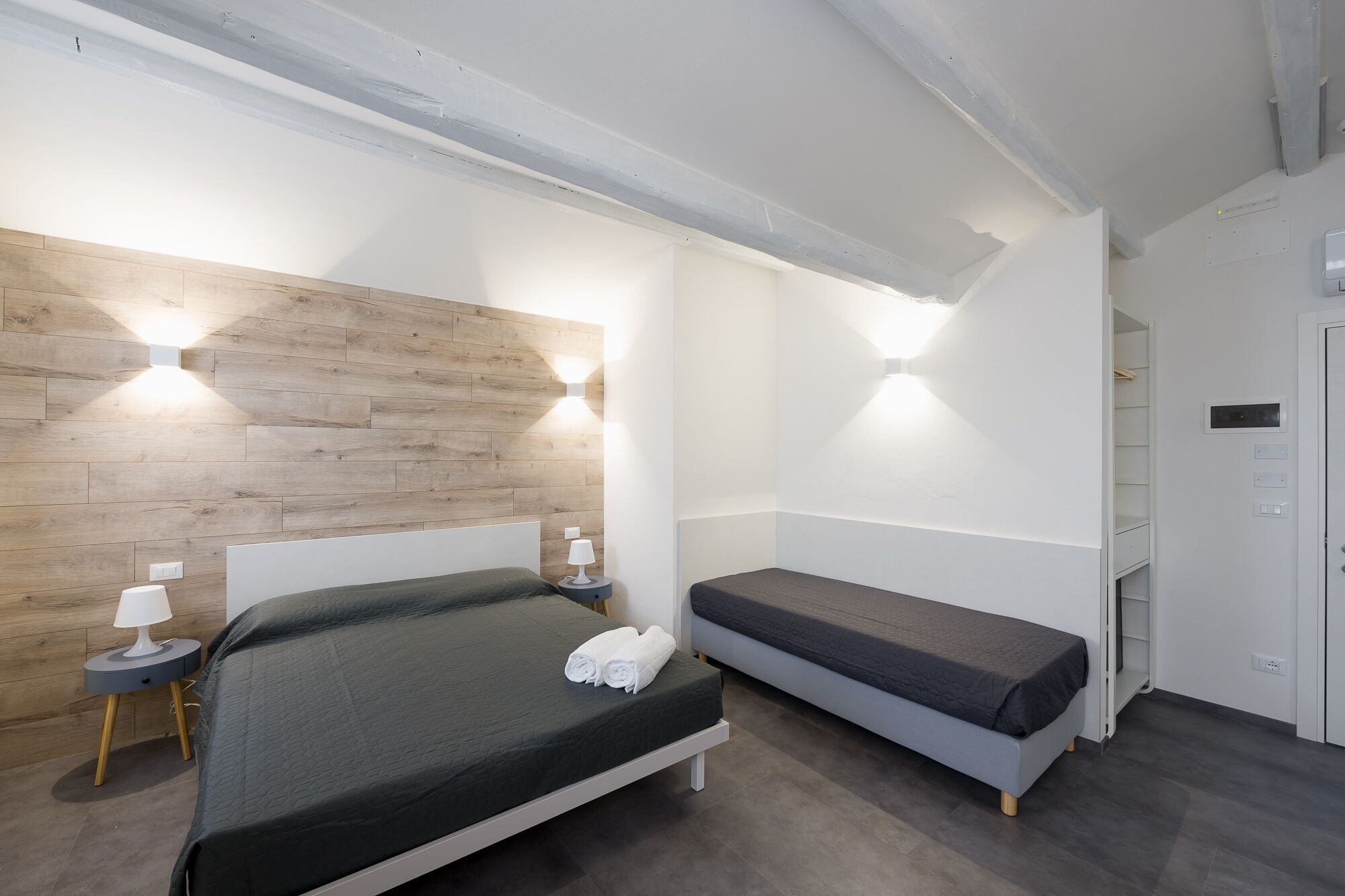 Una habitación de hotel moderna con una pared decorativa de madera, dos camas, lámparas de noche y un armario empotrado.