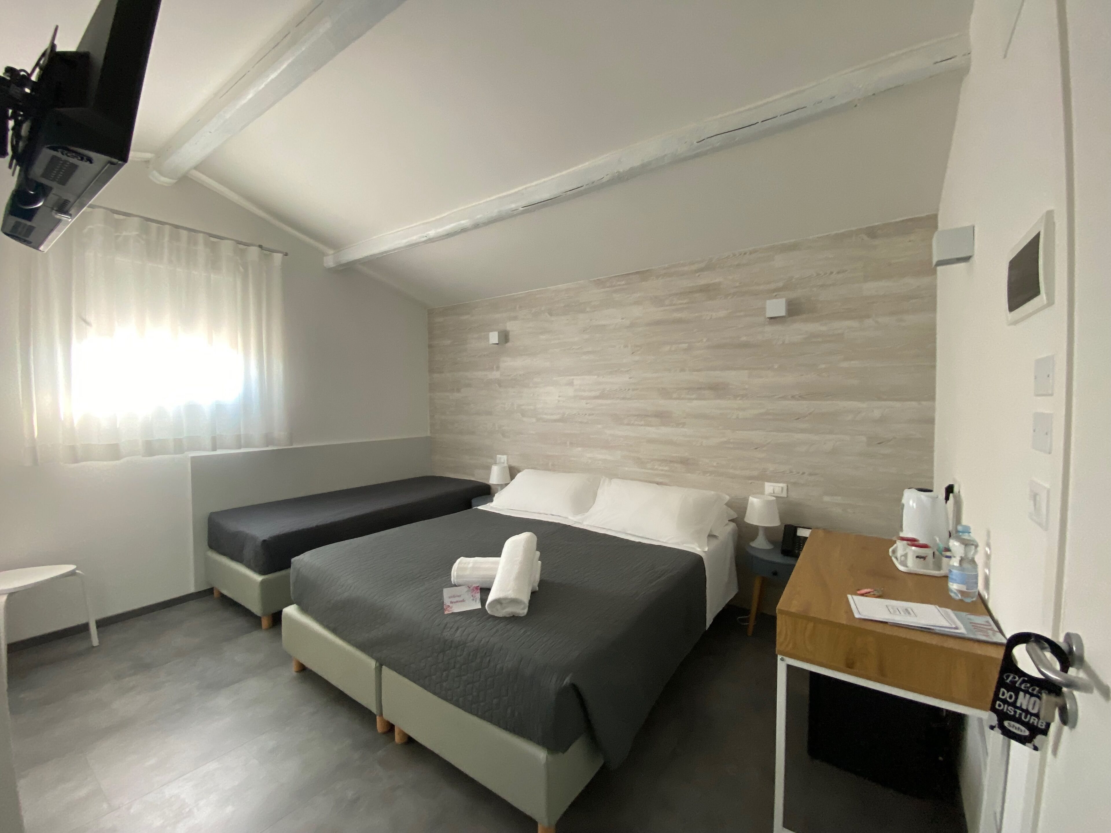 Une chambre d’hôtel avec un grand lit, un lit plus petit, un bureau avec une chaise, une télévision et une fenêtre avec des rideaux.