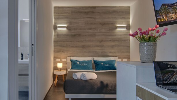 A modern hotel room with a bed, a nightstand, a laptop, and a vase of flowers.