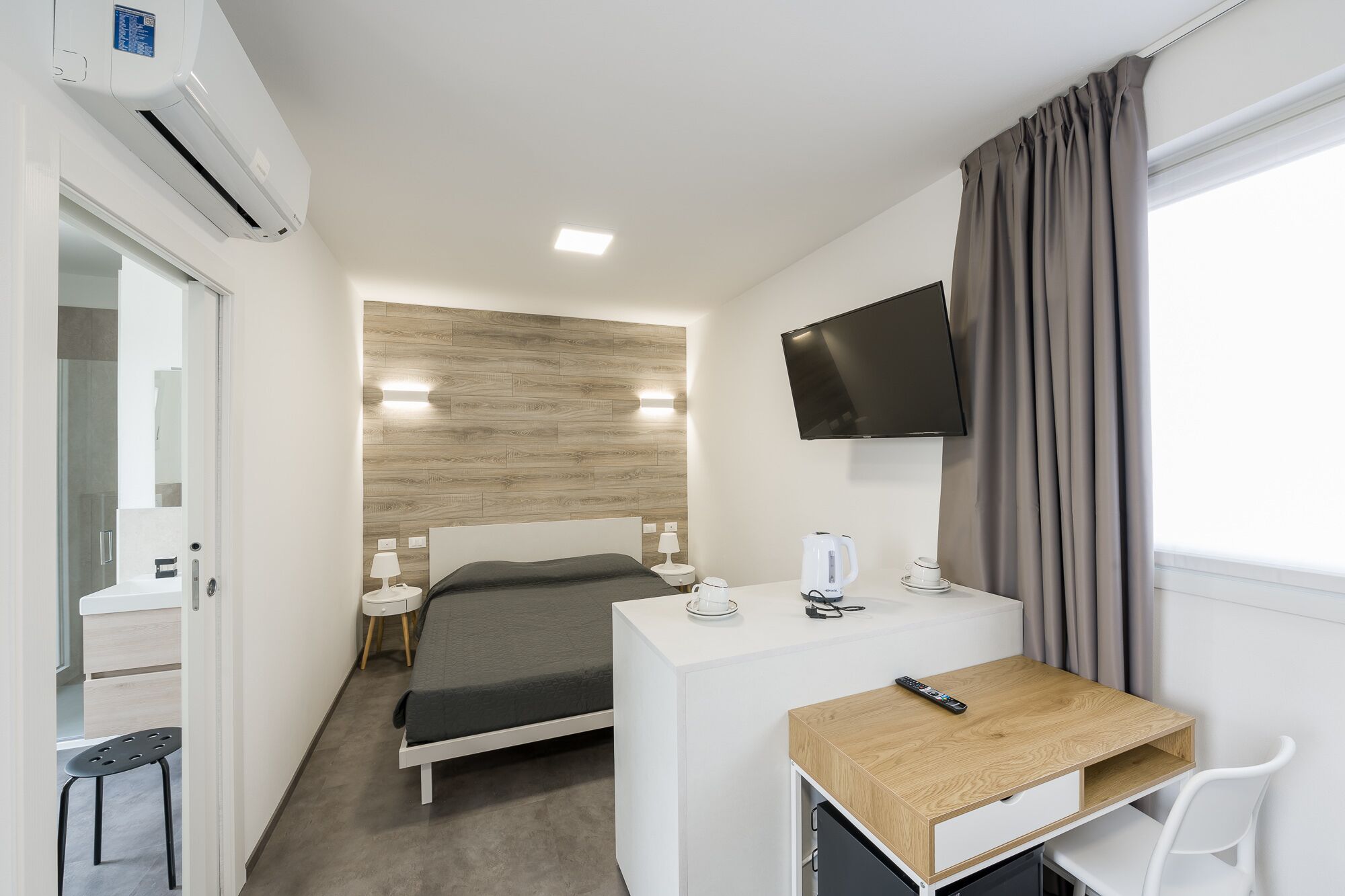Ein Hotelzimmer mit Bett, Nachttisch, Fernseher und Schreibtisch mit Stuhl.