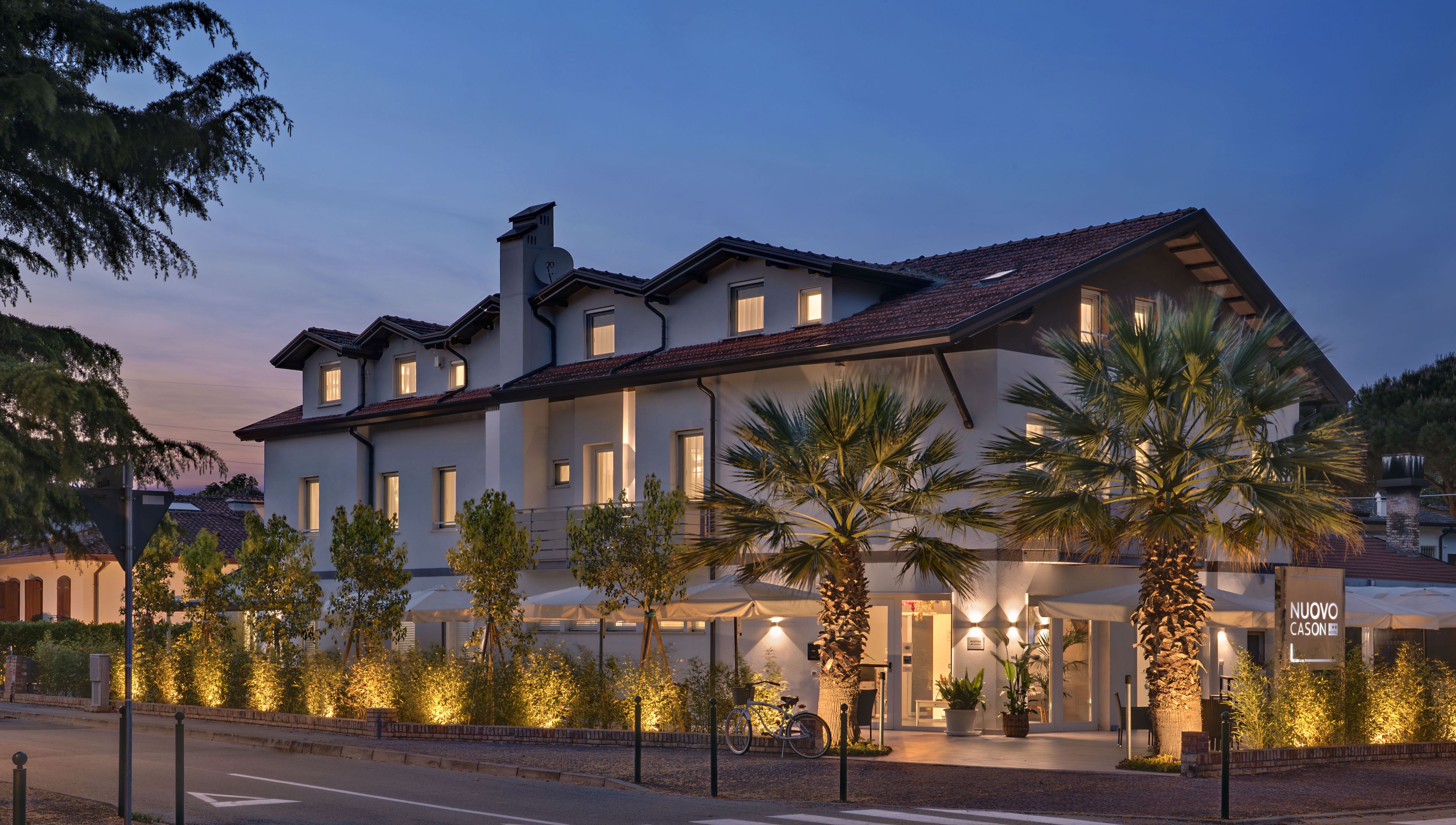 A multi-story hotel with a prominent clock tower, well-lit windows, and a landscaped front with palm trees.