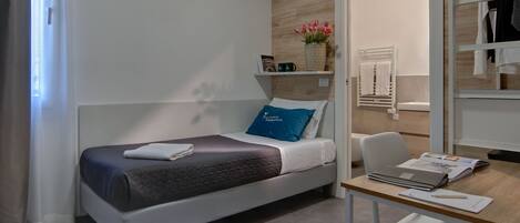 Una cama individual con un almoháron azul, una mesita de noche con un cuaderno, bolígrafo y una computadora portátil.