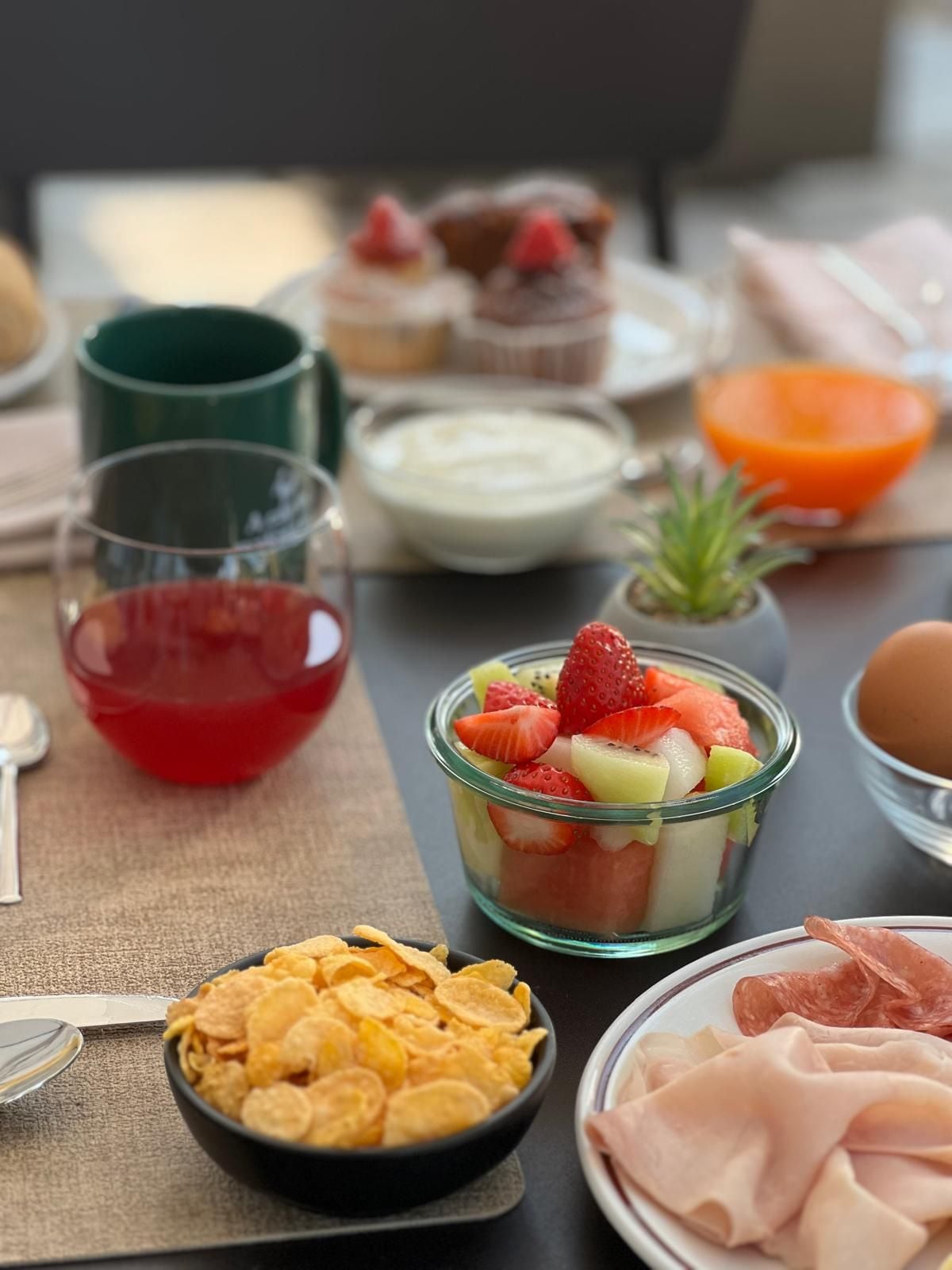 Een tafel met diverse etenswaren, zoals een fruitsalade, ontbijtgranen en vleesschotel.