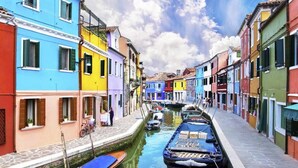 A narrow canal flanked by colorful buildings with a row of boats docked along the water.