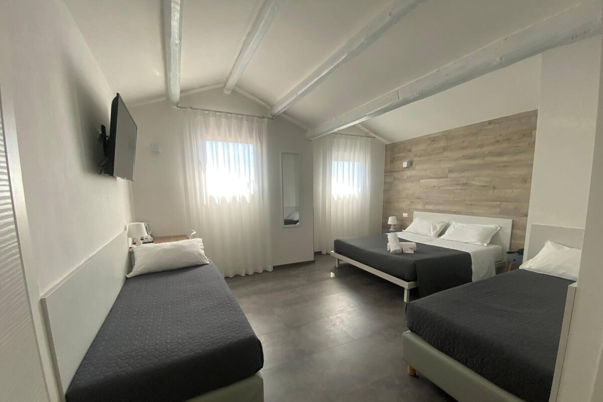 Habitación de hotel con dos camas individuales, un escritorio, una silla, un televisor montado en la pared y una pared decorativa de madera.