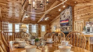 Una sala da pranzo in legno con camino in pietra, un lampadario e un televisore montato a parete.