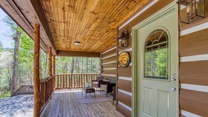 Un portico in legno con una porta verde, un piccolo angolo relax e un cartello che indica un rifugio.