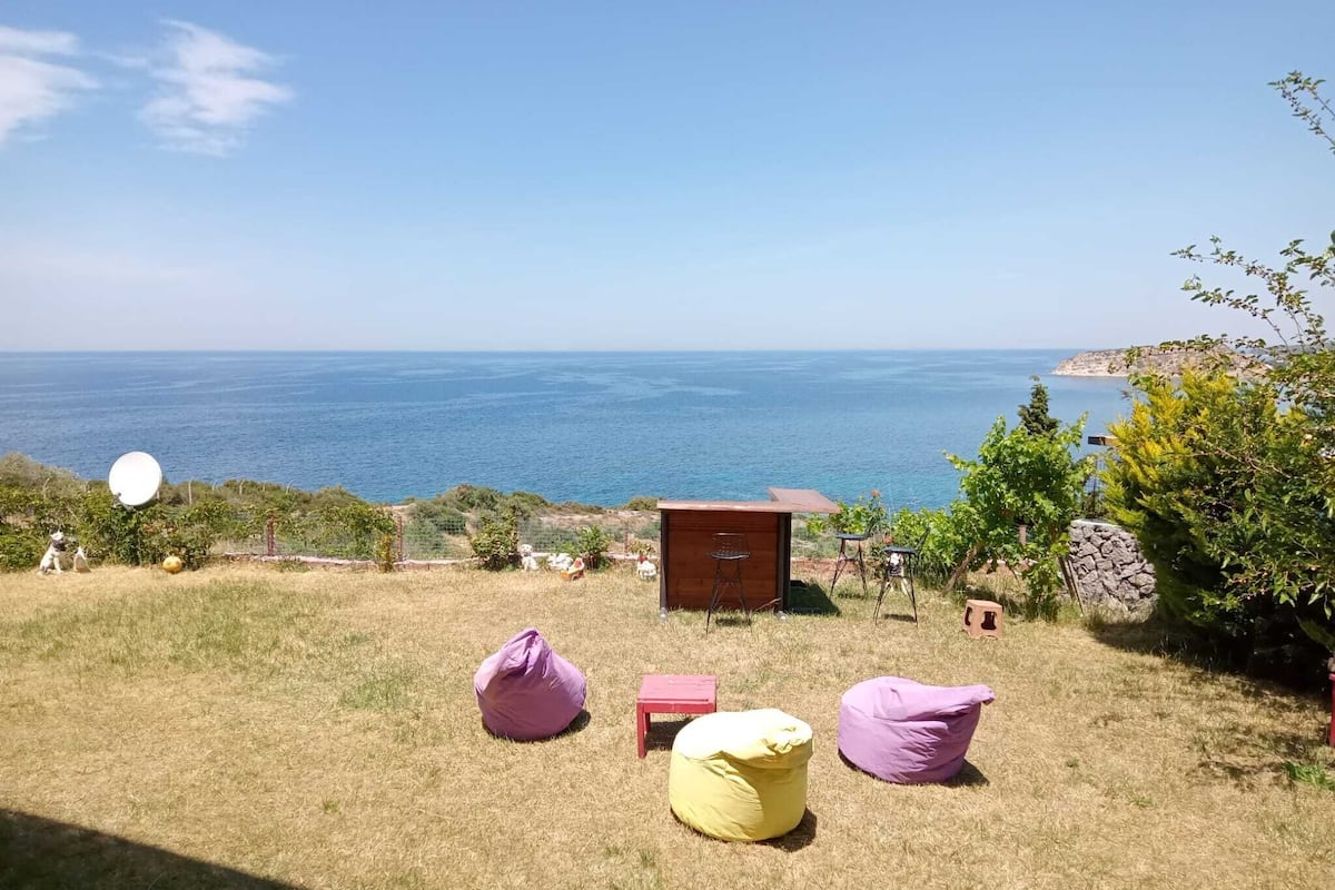 A grassy outdoor area with a wooden structure, two bean bags, and a view of the sea.