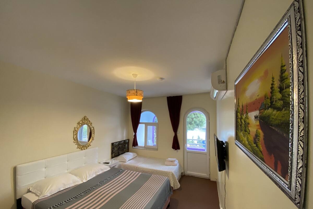 A hotel room with two beds, a large mirror, a painting, and a window with curtains.